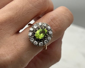May include: A gold ring with a large green peridot gemstone surrounded by a halo of smaller diamonds.