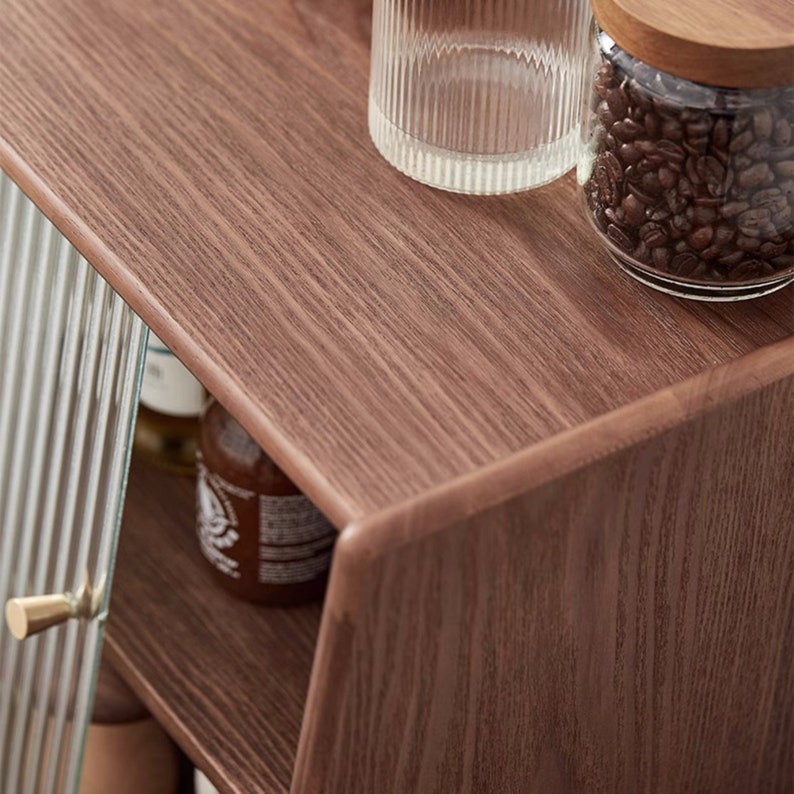 May include: A wooden cabinet with a glass door and shelves. The cabinet has a brown woodgrain finish and is decorated with a glass jar of coffee beans and a glass jar with a wooden lid.