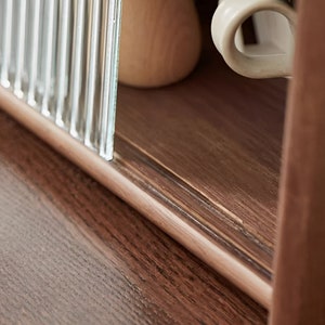 May include: Close-up of a wooden cabinet with a glass door. The cabinet has a dark brown finish and a light brown wood grain. The glass door is made of clear glass with vertical lines.