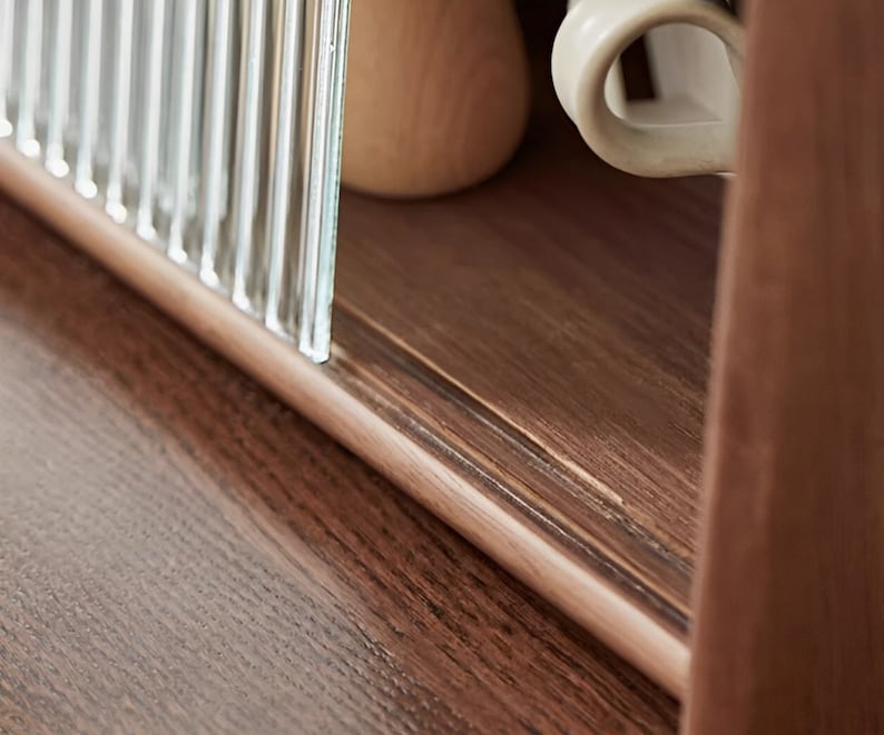 May include: Close-up of a wooden cabinet with a glass door. The cabinet has a dark brown finish and a light brown wood grain. The glass door is made of clear glass with vertical lines.
