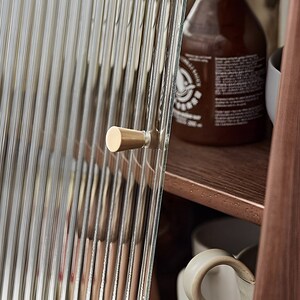 May include: A close-up of a cabinet door with a brass knob. The door is made of clear glass with vertical lines. The cabinet is made of wood.