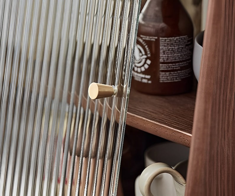 May include: A close-up of a cabinet door with a brass knob. The door is made of clear glass with vertical lines. The cabinet is made of wood.