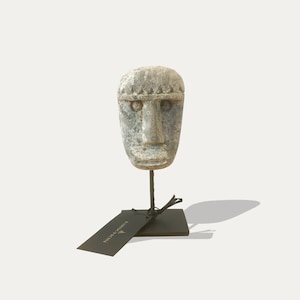 Può includere: Una scultura in pietra grigia di un viso su un supporto in metallo nero con un'etichetta nera che dice "remarkable".