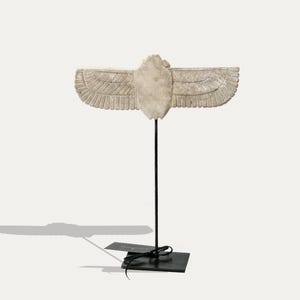 以下が含まれることがあります： 古代メソポタミアのシンボルである、翼のある太陽円盤の白い石膏彫刻。黒い金属製のスタンドの上に置かれています。