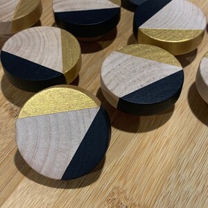 May include: A set of eight round wooden knobs with a geometric design. Each knob is painted black and gold with a triangular pattern.