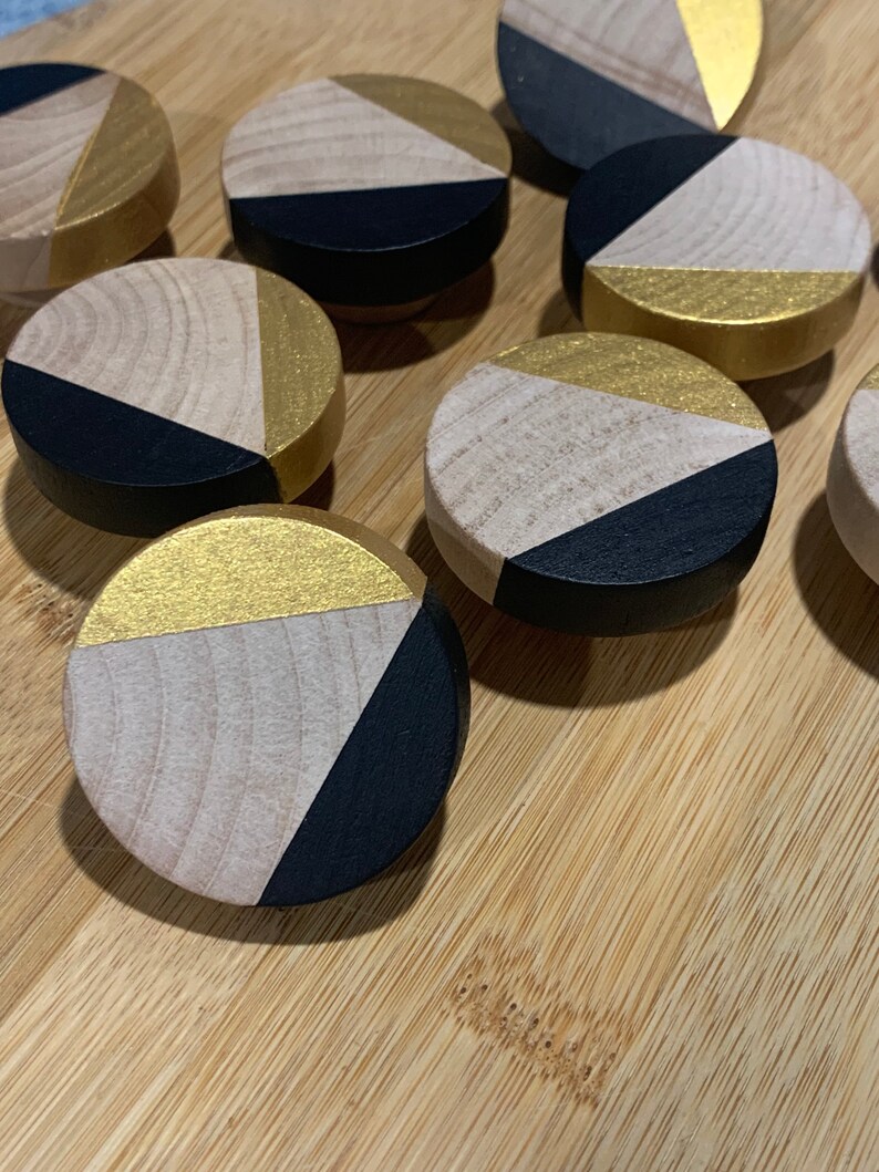 May include: A set of eight round wooden knobs with a geometric design. Each knob is painted black and gold with a triangular pattern.