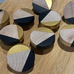 May include: Nine round wooden knobs with a geometric design. Each knob is painted black and gold with a triangular pattern.