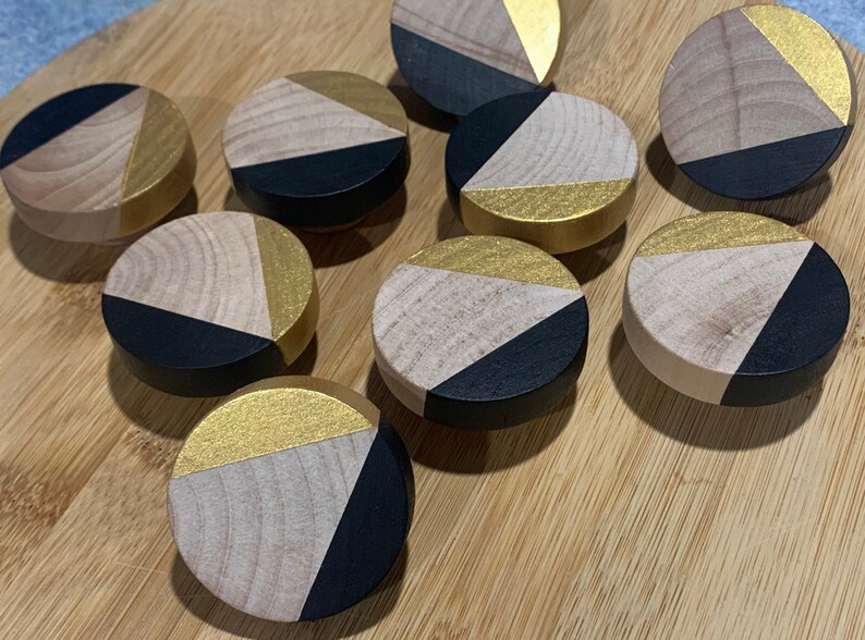 May include: Nine round wooden knobs with a geometric design. Each knob is painted black and gold with a triangular pattern.