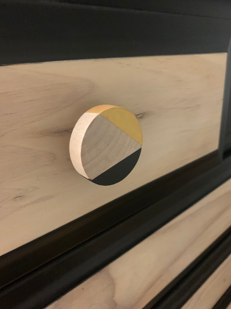 May include: A round wooden drawer knob with a geometric design in black, gold, and natural wood.