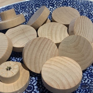 May include: A collection of round wooden knobs in various sizes, all in a natural wood colour. The knobs are arranged in a pile on a blue and white patterned surface.