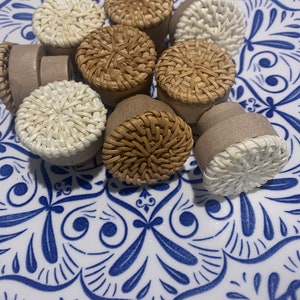 May include: A collection of eight woven rattan knobs in various shades of brown and white. The knobs are arranged on a white plate with a blue and white floral pattern.