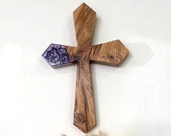Può includere: Una croce di legno con un'intarsio di cristallo di ametista viola. La croce è realizzata in legno d'ulivo e ha un aspetto rustico e naturale.