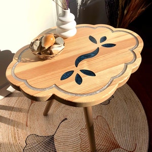 May include: A wooden side table with a unique cloud-shaped top and three legs. The top features a blue floral design and a white border.