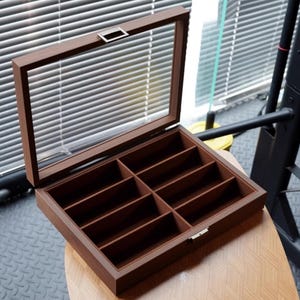 May include: A wooden box with a glass lid and eight compartments. The box is brown and has a silver latch.