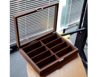 May include: A wooden box with a glass lid and eight compartments. The box is brown and has a silver latch.