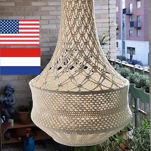 Puede incluir: Una pantalla de lámpara de crochet blanco colgada del techo de un balcón. La pantalla está hecha de un patrón delicado y de tejido abierto. El fondo muestra una pared de ladrillo y una planta en maceta.
