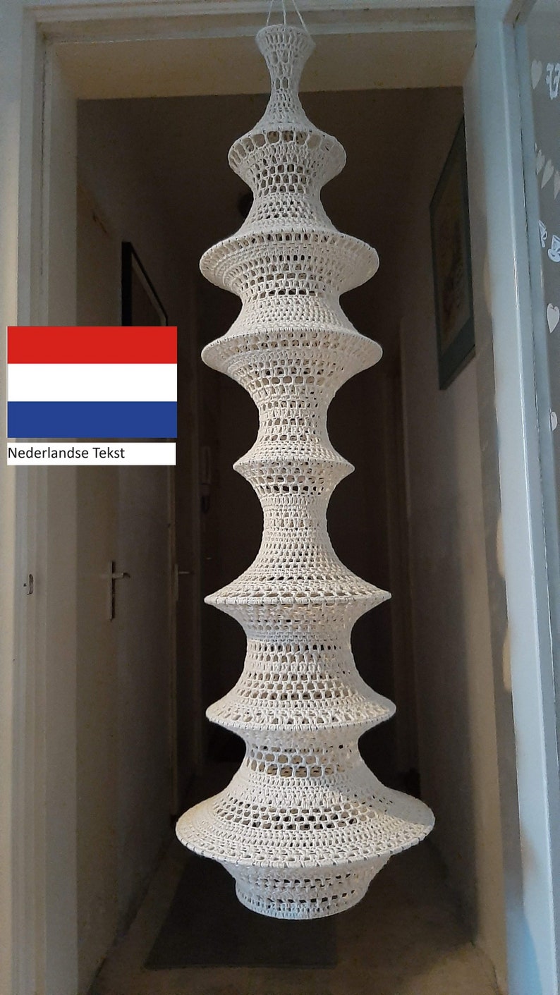 May include: A white crocheted lampshade with a tiered design hangs from the ceiling. The lampshade is made of a delicate, openwork pattern.