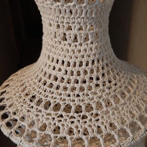 May include: A white crocheted lampshade with a tiered design. The lampshade is made of a delicate, openwork pattern.