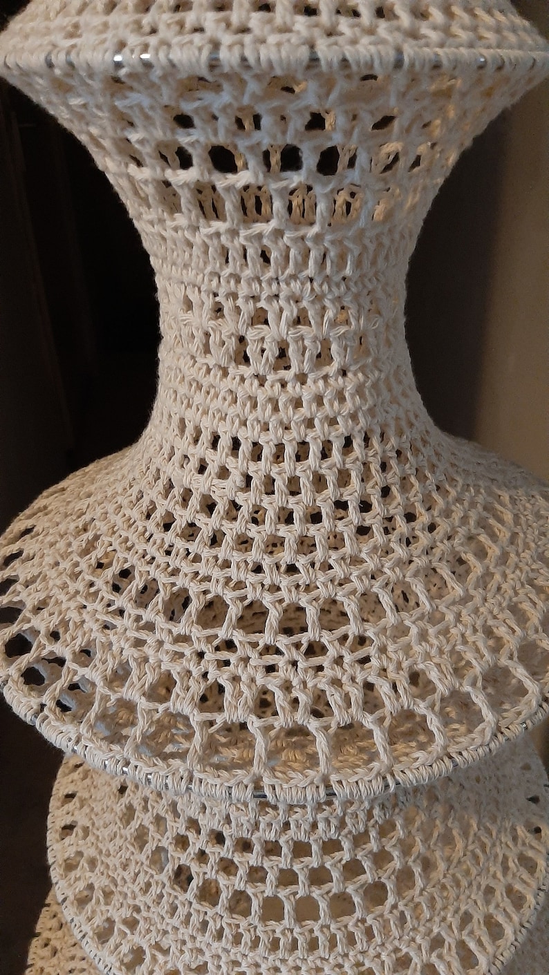 May include: A white crocheted lampshade with a tiered design. The lampshade is made of a delicate, openwork pattern.