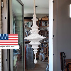 Peut inclure: Un luminaire suspendu en crochet blanc. Le luminaire a une forme allongée à plusieurs niveaux avec un pompon en bas. Le luminaire est suspendu au plafond, mettant en valeur un design bohème unique. Le luminaire est en crochet.