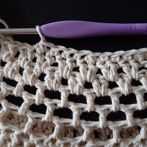 May include: Close-up of a crocheted piece in a cream color with a purple crochet hook resting on top. The crochet hook is 4.5 mm.