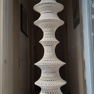 May include: A white crocheted lampshade with a tiered design. The lampshade is hanging from the ceiling and is made of a delicate, openwork pattern.