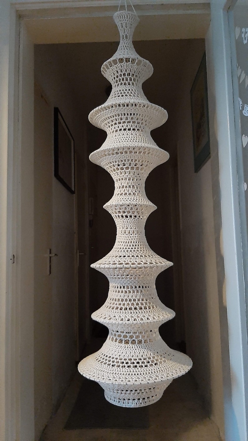May include: A white crocheted lampshade with a tiered design. The lampshade is hanging from the ceiling and is made of a delicate, openwork pattern.