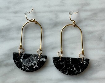 May include: A pair of gold hoop earrings with black and white marbled half-circle pendants.