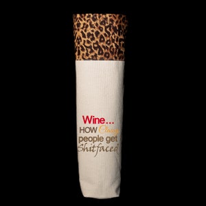 May include: A white canvas wine bottle bag with a leopard print top. The bag has the text "Wine... How classy people get shitfaced" printed on it.