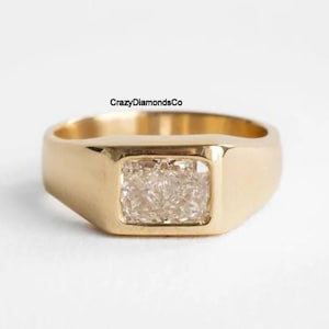 May include: A gold signet ring with a square-shaped clear diamond set in the center.