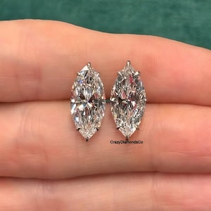 Puede incluir: Un par de pendientes de diamantes de talla marquesa en un engaste de plata. Los pendientes están en una mano.