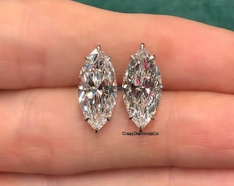 May include: A pair of marquise cut diamond earrings in a silver setting. The earrings are on a hand.