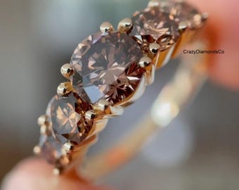 May include: A gold ring featuring a row of five round-cut brown diamonds set in prongs. The band is thin and metallic, and the text CrazyDiamondsCo is visible in the upper right corner of the image, near the stones.