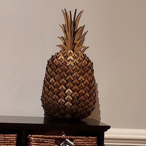 May include: A large, golden pineapple sculpture crafted from wood. The pineapple is intricately detailed with individual scales and a leafy crown.