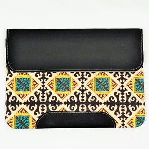 Könnte beinhalten: Eine schwarze Leder-Laptoptasche mit einem gemusterten Stoffklappen. Der Stoff hat ein geometrisches Muster in Gelb-, Blau- und Schwarztönen.