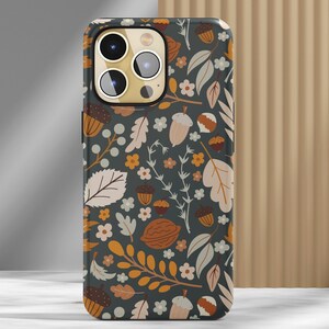 May include: A smartphone case with a fall-themed design. The case features a dark gray background adorned with illustrations of acorns, leaves, and flowers in shades of brown, orange, and cream. The case has a glossy finish and a camera cutout.