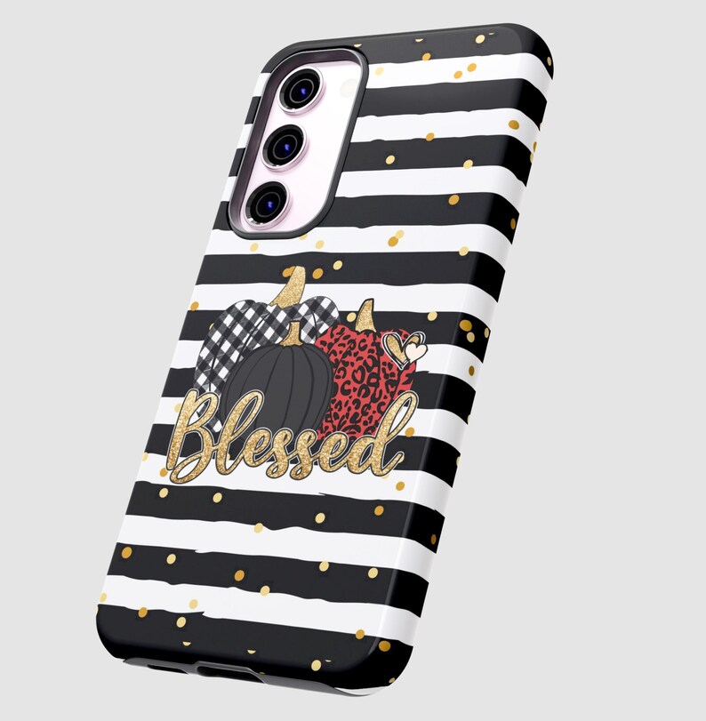 Puede incluir: Funda de tel&eacute;fono a rayas blancas y negras con purpurina dorada y un dise&ntilde;o de tres calabazas con la palabra "Blessed" en purpurina dorada.
