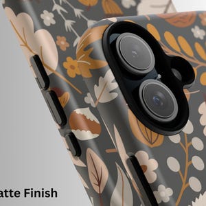 May include: Close-up of a smartphone case with a matte finish. The case features a floral pattern in shades of gray, beige, and orange. The design includes leaves, flowers, and other botanical elements. The text "Matte Finish" is visible at the bottom.