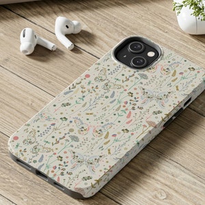 Puede incluir: Una funda de tel&eacute;fono blanca con un patr&oacute;n floral con mariposas y peque&ntilde;as flores. La funda tiene un recorte para el objetivo de la c&aacute;mara y un fondo crema.