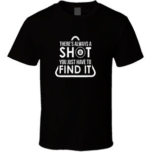 Può includere: T-shirt nera con testo bianco: "THERE'S ALWAYS A SHOT, YOU JUST HAVE TO FIND IT." La parola "SHOT" presenta una grafica della palla numero 8. La maglietta è in stile girocollo classico.