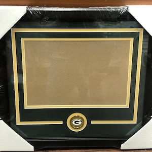May include: A black and green picture frame with a gold mat and a gold and green Green Bay Packers logo in the bottom center.