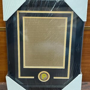 May include: A black framed picture with a gold mat and a gold circular emblem with a yellow "P" in the center. The emblem says "Pittsburgh Pirates" around the outside.