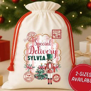 May include: A cream-colored Santa sack with red drawstring and tassels. The sack features a festive design with the text "Special Delivery Sylvia" and a nutcracker illustration. A red circle indicates two sizes are available.