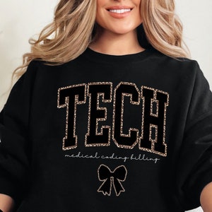 May include: Black sweatshirt with the word "TECH" in large gold letters outlined in black. The letters are decorated with a leopard print pattern. Below the word "TECH" is the text "medical coding billing" in smaller white letters. A black bow with gold leopard print accents is below the text.