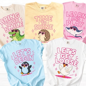 May include: Five short-sleeve t-shirts in ivory, yellow, pink, light blue, and white. Each shirt features a cartoon animal wearing heart-shaped sunglasses and pink text: Bring Your Smile with a crocodile, Time To Shine with a hedgehog, Learn And Play with a stingray, Let's Begin with a penguin, and Let's Get Loose with a goose.