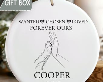 May include: White ceramic ornament with a paw and hand illustration. Text reads "WANTED CHOSEN LOVED FOREVER OURS" and "COOPER 4-15-2025". Includes a "FREE GIFT BOX" graphic. A touching keepsake for pet lovers.