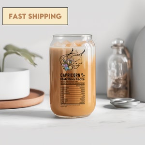 May include: A clear glass can containing a brown liquid. The can features a label that reads "Capricorn Nutrition Facts" and lists various personality traits with percentages. The can is positioned on a white surface.
