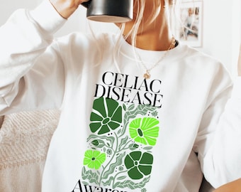 Könnte beinhalten: Weißer Pullover mit grünem und gelbem Blumendesign und dem Text "Celiac Disease Awareness".