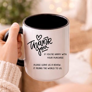 May include: White ceramic mug with a black interior and handle. The mug features the words "Thank you" in a handwritten style, along with the text "If you're happy with your purchase, please leave us a review. It means the world to us."