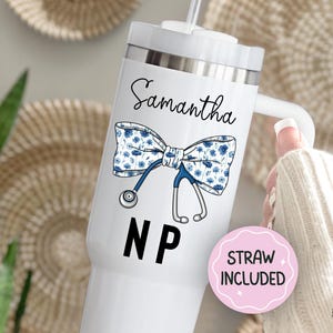 May include: White tumbler with a lid and straw, featuring a blue floral bow tie design and a stethoscope. The name "Samantha" is written above the bow tie, with "NP" below. A pink sticker says "STRAW INCLUDED".